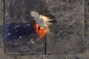 Fire retardant balls dropped by Anduril's Ghost-X drone explode on a fire in a test. The scene from above shows a cloud of fire retardant just spreading out with the blaze beneath it.